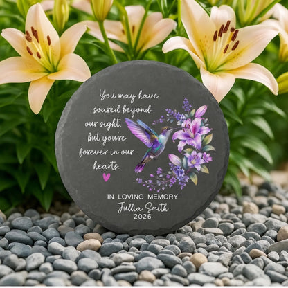 Hummingbird memorial stone among lilies and pebbles